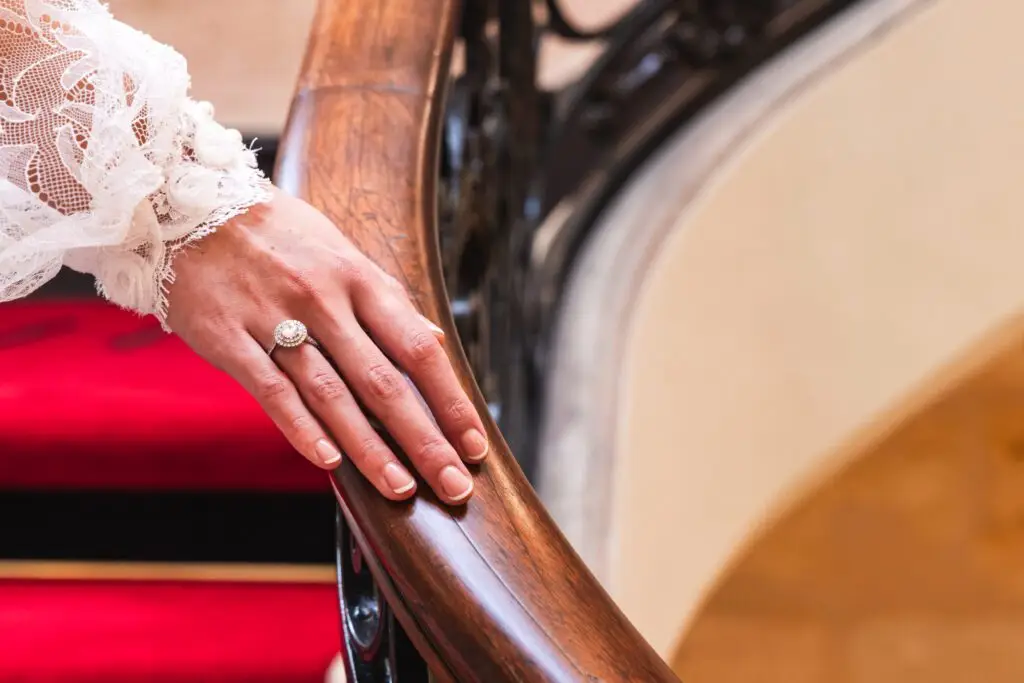 Gros plan sur la main de la modèle posée sur la rampe d'escalier, avec un focus particulier sur la bague en diamant