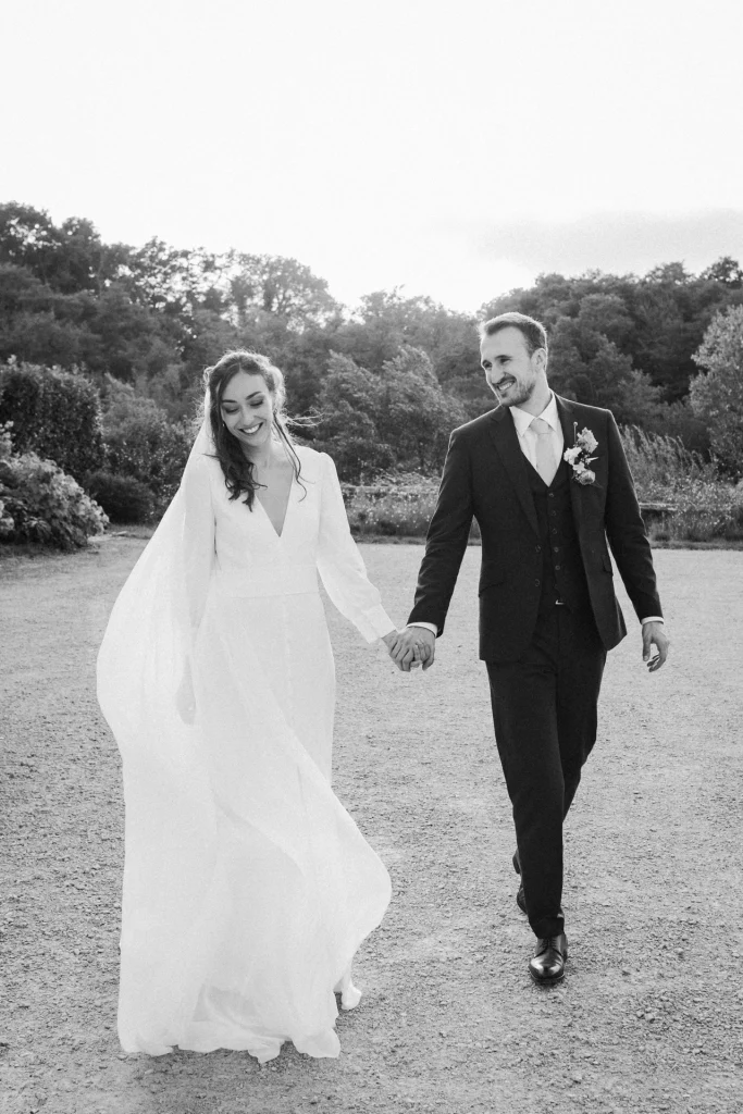 Pendant la séance couple, les mariés marchent main dans la main en souriant, lors de leur mariage dans les Landes immortalisé par une photographe professionnelle.