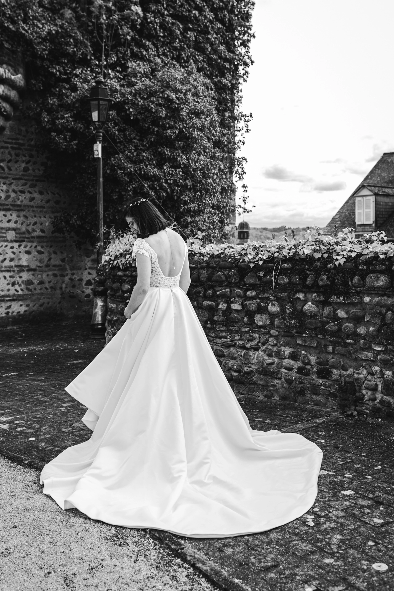 De dos, la mariée observe la longue traîne de sa robe, sur les remparts de Lescar dans les Pyrénées Atlantiques