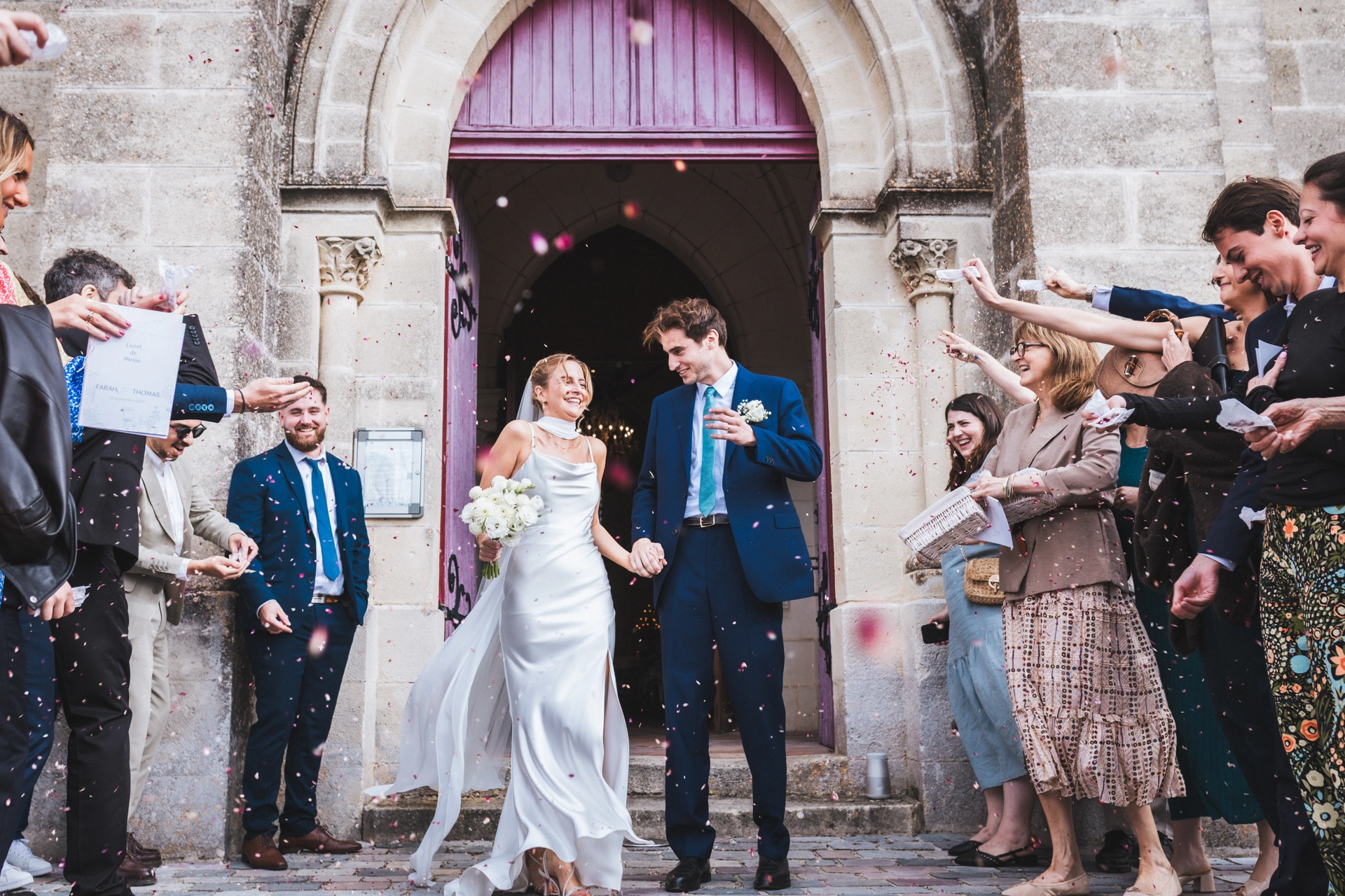 Sortie de cérémonie religieuse sous les pétales de fleurs lors d'un mariage coloré en Gironde
