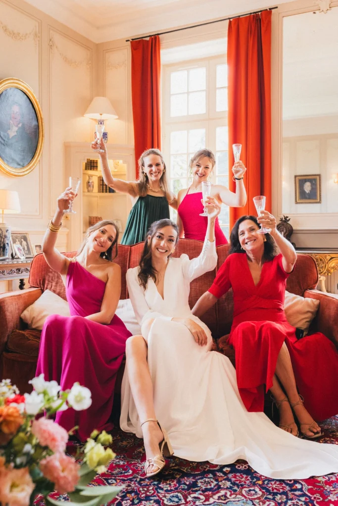 La mariée, sa mère et ses demoiselles d'honneur prennent la pose avec une coupe de champagne sur un canapé, dans le salon du château de Campet dans les Landes.