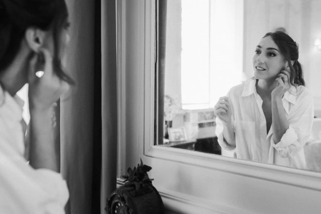 La mariée se regarde dans le miroir après avoir été coiffée et maquillée, et essaie ses boucles d'oreilles, dans le salon du château de Campet dans les Landes.