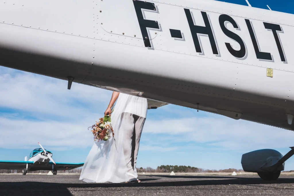 Un avion cache en partie la mariée, dont on n'aperçoit que le bouquet, les jambes et la robe, à l'aérodrome de Sarlat en Dordogne.