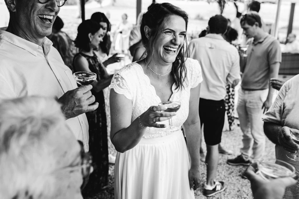 Portrait de la mariée qui rit aux éclats, un verre de champagne à la main, pendant son cocktail de mariage en Dordogne.