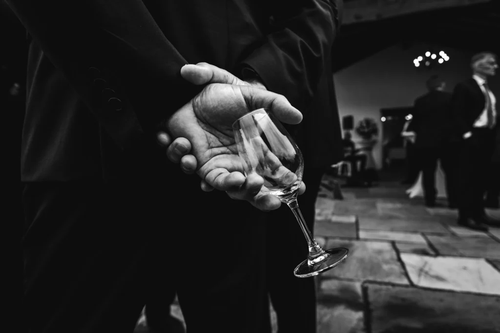 Détail des mains d'un invité tenant un verre vide, lors d'un cocktail de mariage à la Ferme aux Piments au Pays Basque.
