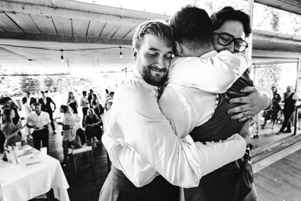 Les mariés enserrent dans leur bras un invité après son discours plein d'émotion pendant le cocktail de mariage à Bordeaux.