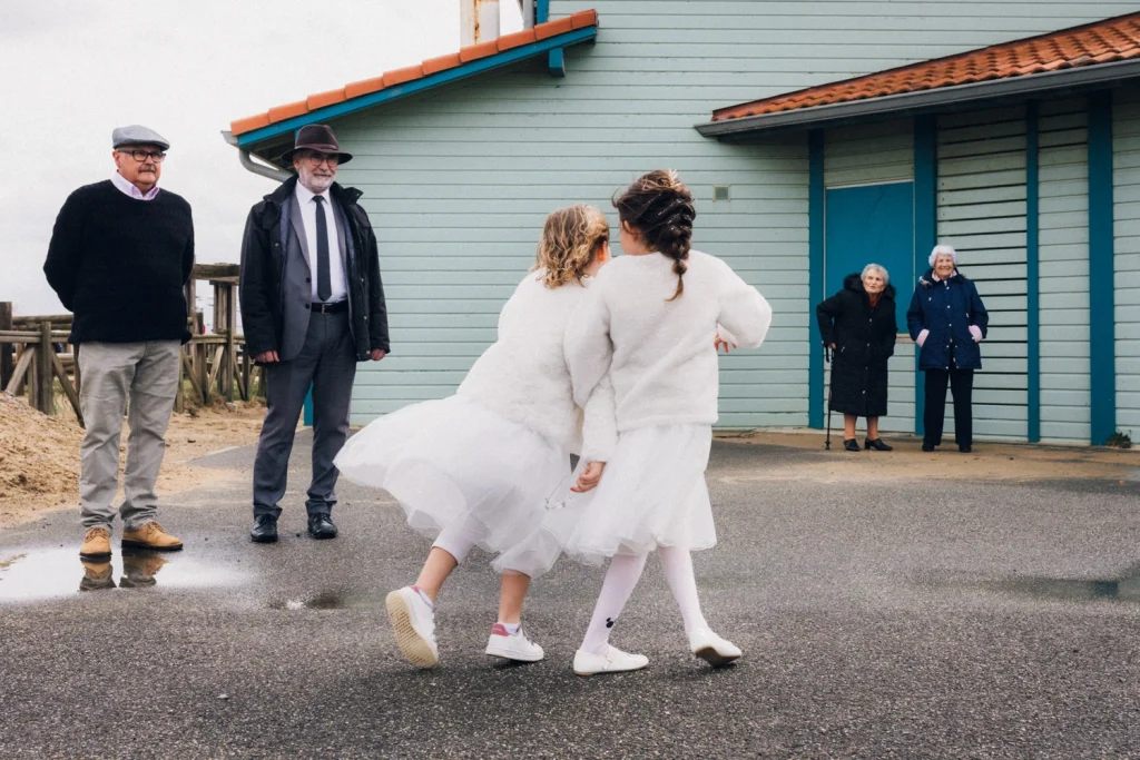 Deux petites filles se tiennent la main sur le front de mer alors que les grands-parents les regardent, lors d'un mariage dans les Landes à Lit-et-Mixe.