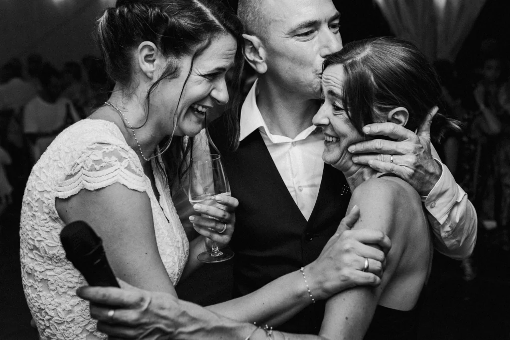 Moment de tendresse entre les mariés et une de leurs amies, qui la serrent dans leur bras après un discours touchant pendant le repas de mariage en Dordogne.