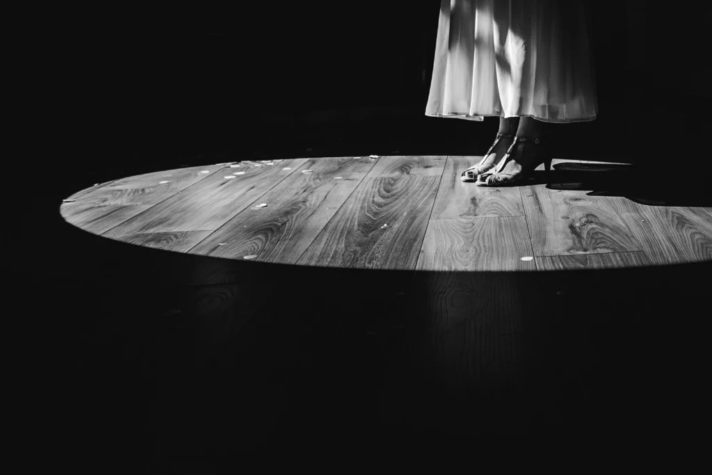 Détail des pieds et du bas de la robe de la mariée dans un cercle de lumière, alors qu'elle s'apprête à danser pour son ouverture de bal.
