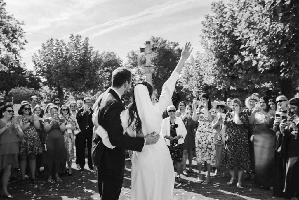 Sortie d'église sous le soleil des Landes, les mariés de dos saluent leur foule d'invités.