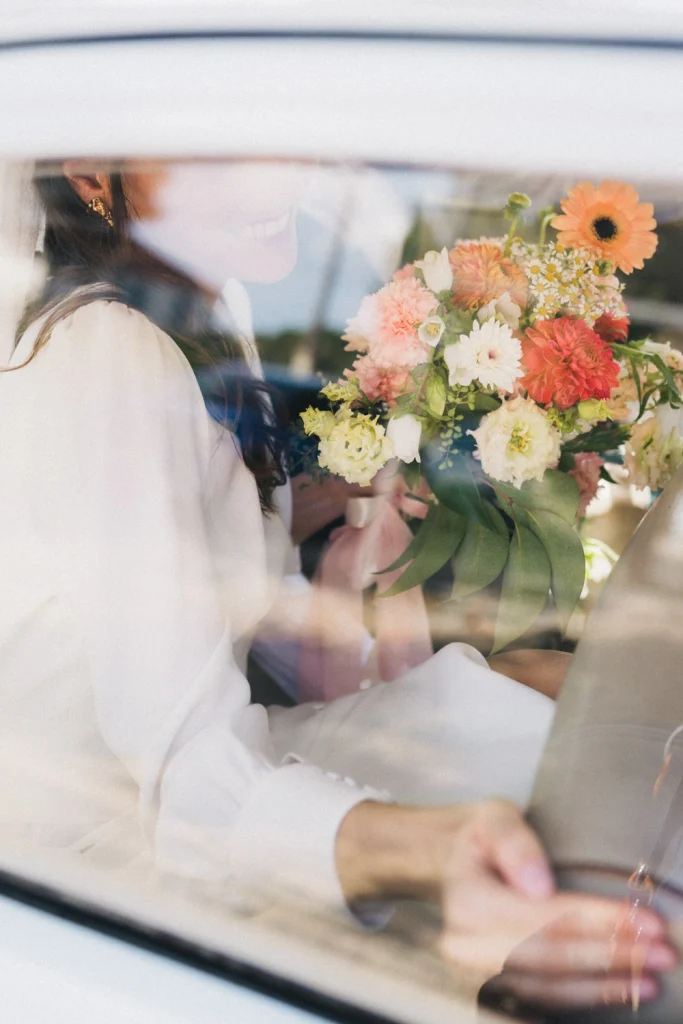 A travers la vitre de la voiture, la mariée sourit en tenant son bouquet, alors qu'elle se dirige vers le domaine de mariage dans les Landes.