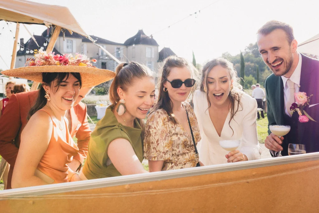 Les mariés et des invités regardent un tableau sur lequel sont accrochés des photos de leur enfance, par une photographe mariage landes.