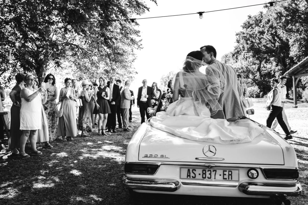 Les mariés arrivent dans leur voiture de collection sur le lieu du cocktail et s'embrassent pendant que les invités les prennent en photo dans les Landes.