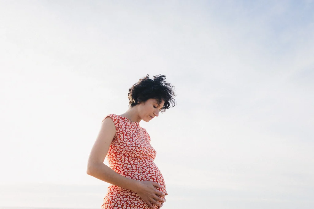 Séance grossesse au bord de l'eau, la future maman caresse doucement son ventre rond.