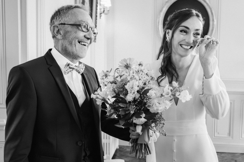 La mariée s'essuie délicatement une larme, après que son père l'ait découverte en robe de mariée dans le salon du château de Campet