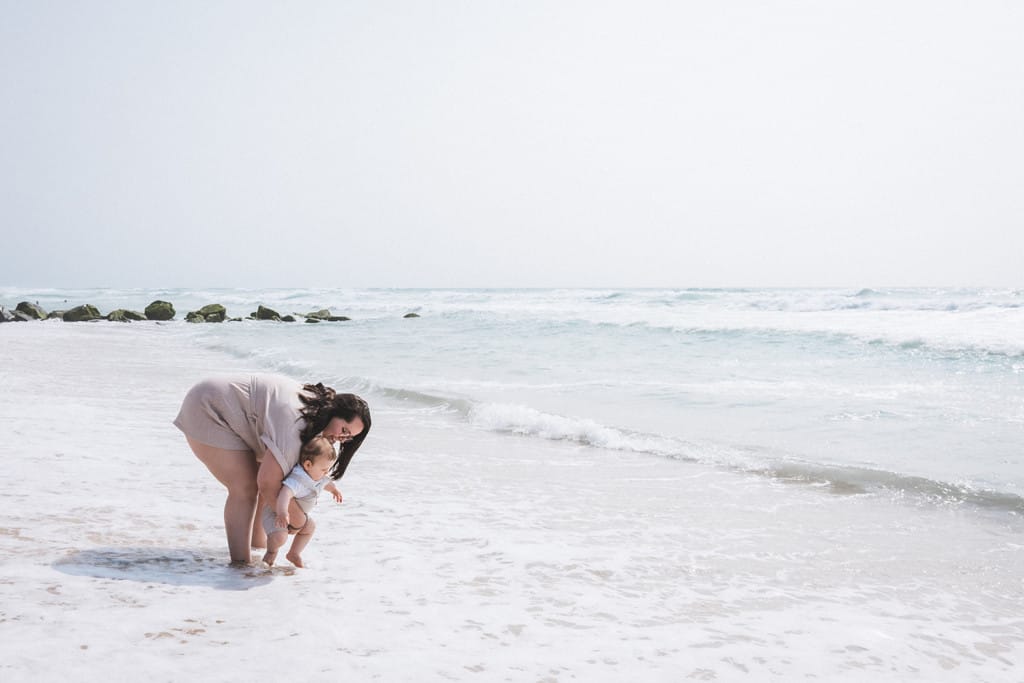 Une mère accompagne son bébé au bord de l'eau et lui fait tremper les pieds dans l'eau, par une photographe famille landes