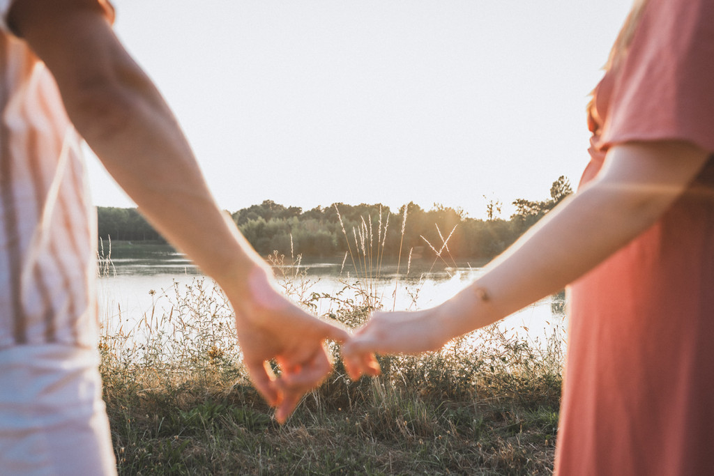 Détail des mains enlacées du couple avec un lac en toile de fond