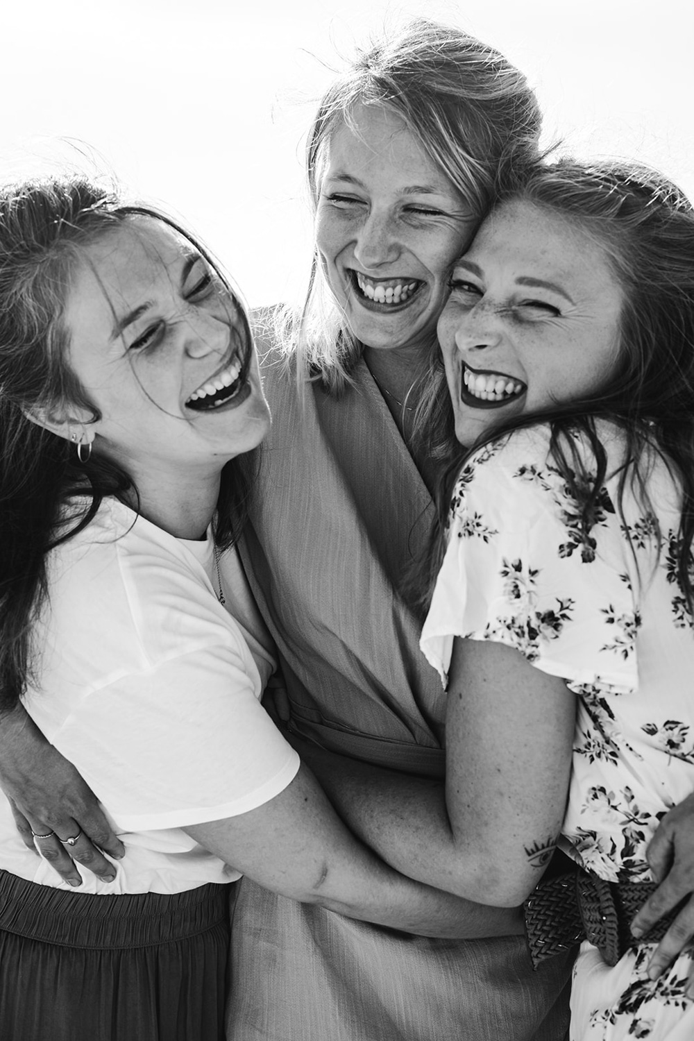 Lors d'une séance photo famille en Gironde, trois soeurs s'enlacent en riant sur la plage?