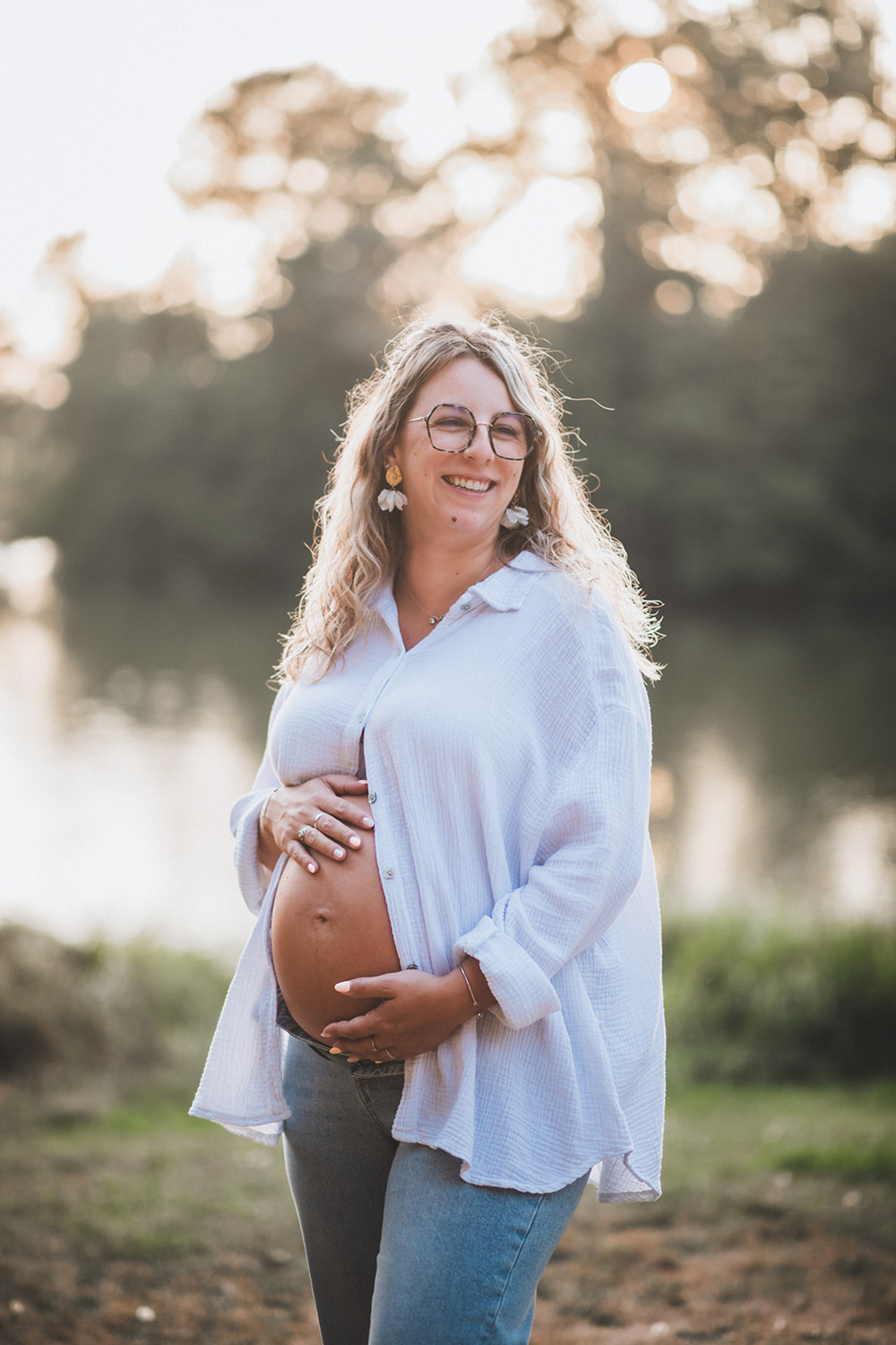 La future maman, tenant délicatement son ventre dans les mains, regarde vers son compagnon en souriant