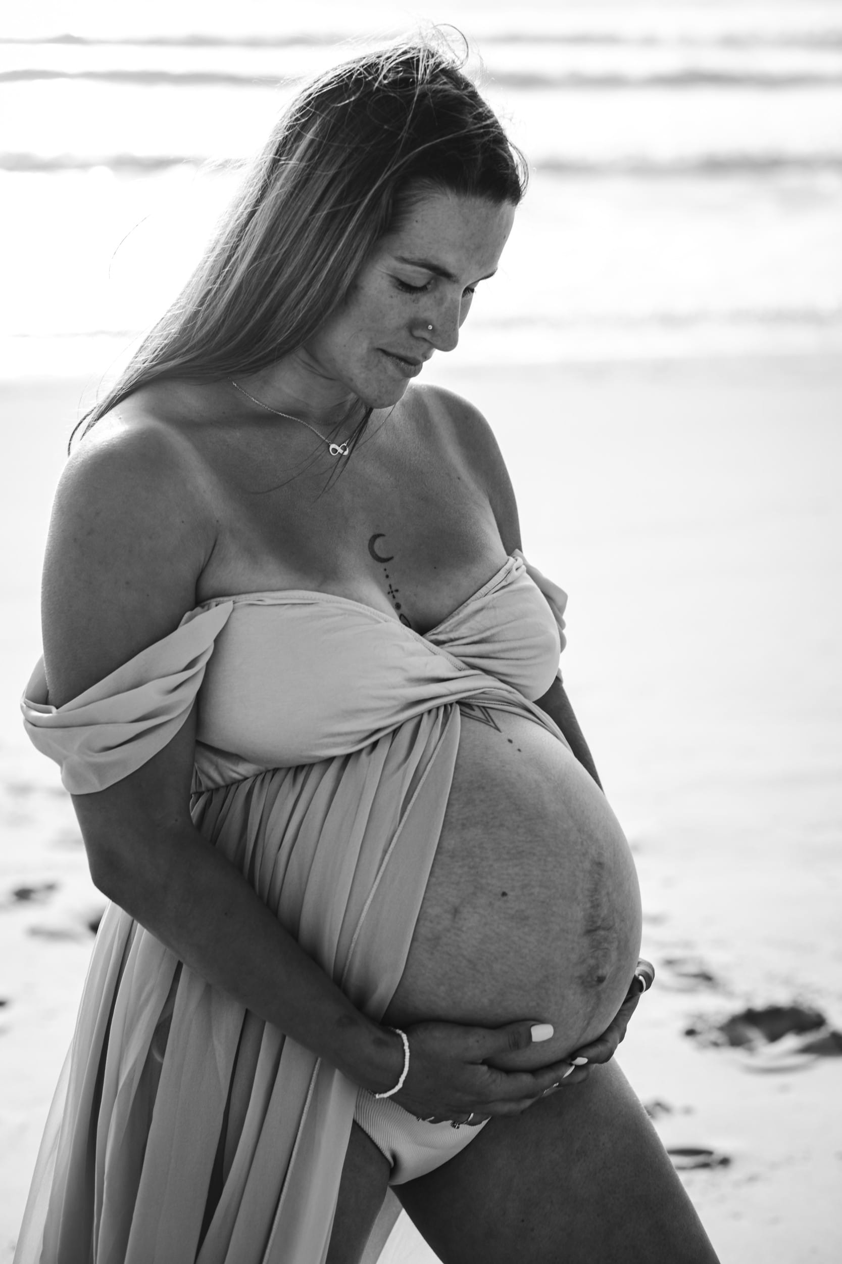 La future maman tient délicatement son ventre et regarde vers son futur bébé, par une photographe grossesse bordeaux