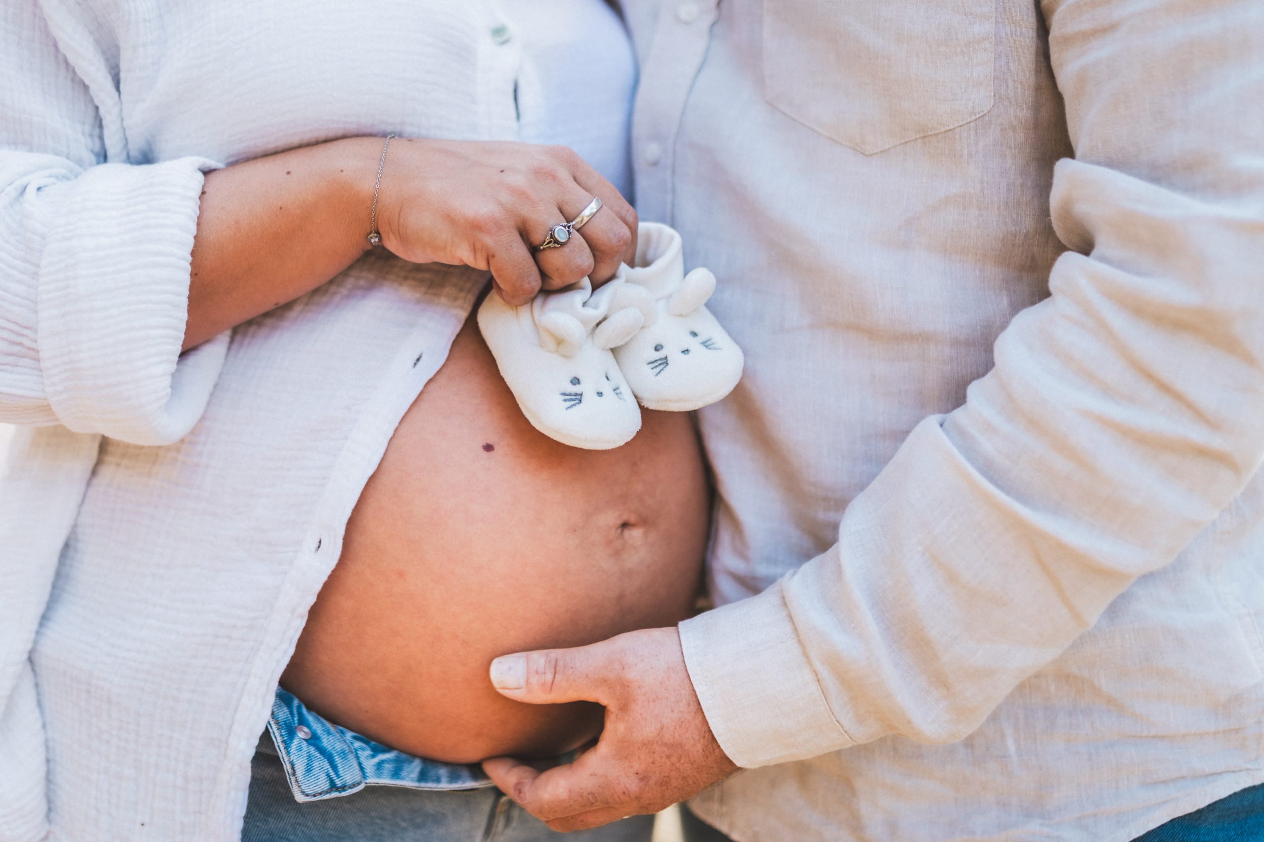 Gros plan sur le ventre rond et les petits chaussons tenus par la future maman lors d'une séance grossesse dans les Landes