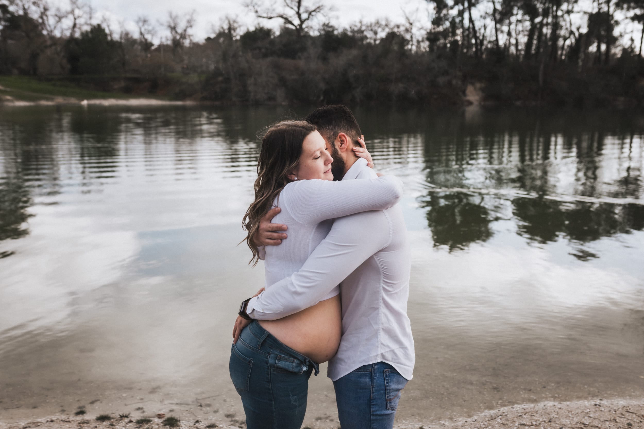 Les futurs parents s'enlacent au bord d'un lac durant leur séance avec une photographe grossesse Bordeaux à Léognan