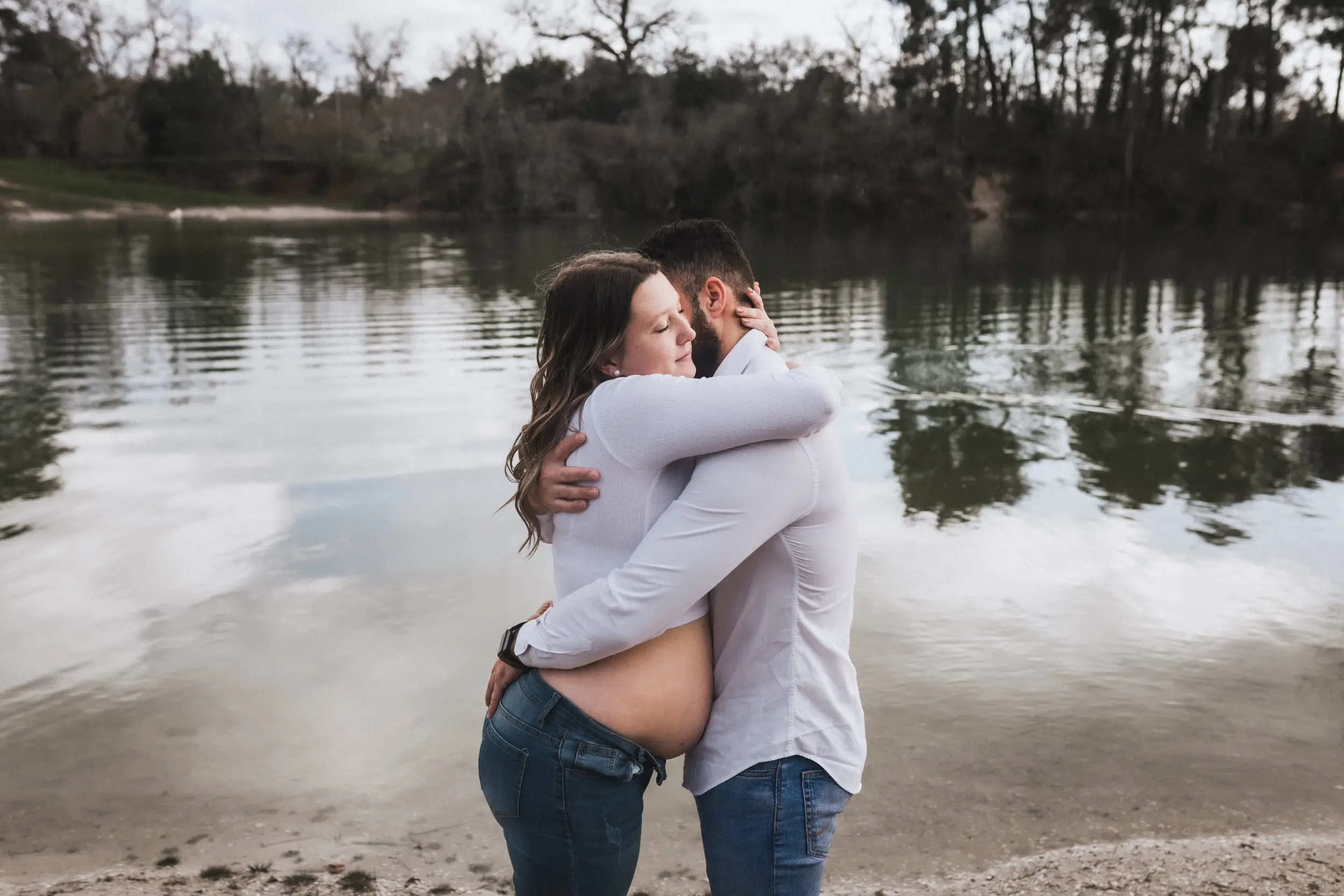 Les futurs parents s'enlacent au bord d'un lac durant leur séance avec une photographe grossesse Bordeaux à Léognan