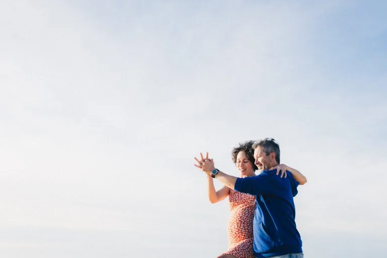 Les futurs parents dansent une valse, avec le ciel bleu en fond, durant leur séance grossesse à Lacanau
