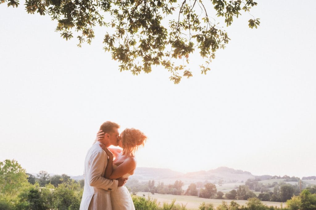 Durant leur séance photo de mariage au château Sainte-Foy, les mariés s'embrassent tendrement dans la lumière du soleil couchant