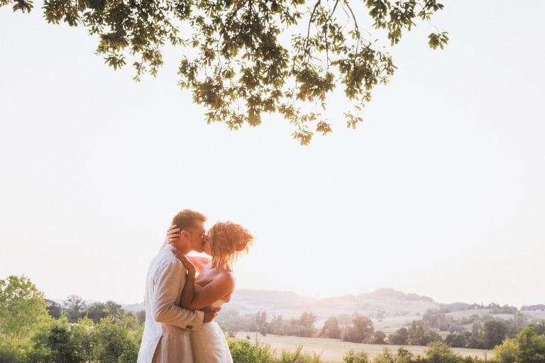Durant leur séance photo de mariage au château Sainte-Foy, les mariés s'embrassent tendrement dans la lumière du soleil couchant