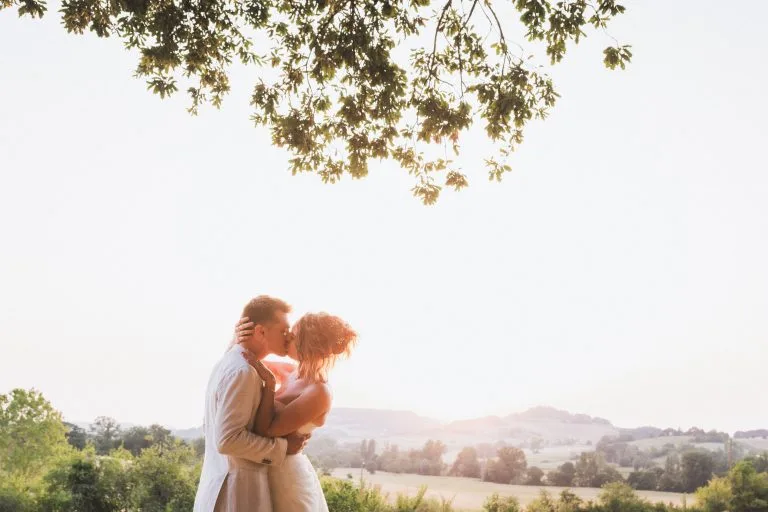 Durant leur séance photo de mariage au château Sainte-Foy, les mariés s'embrassent tendrement dans la lumière du soleil couchant