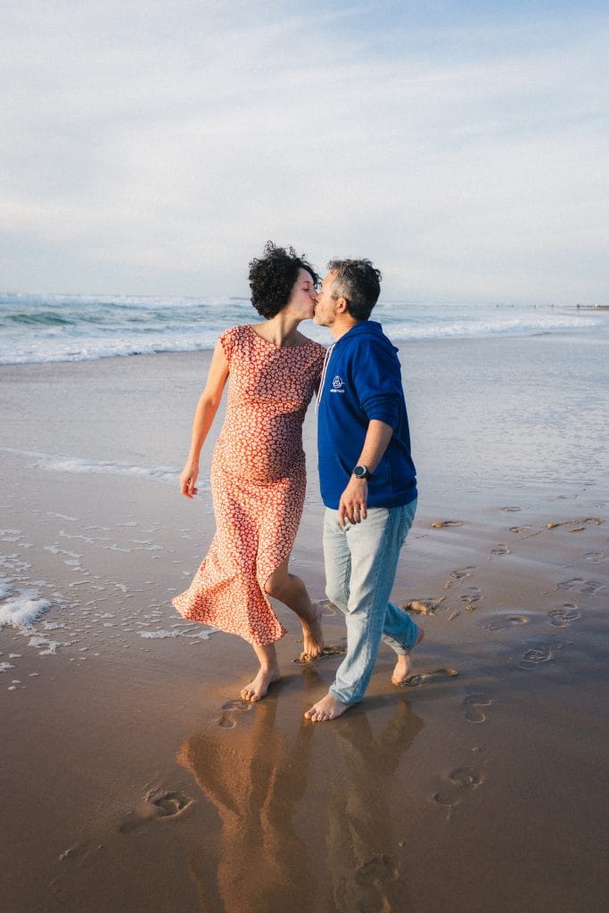 Les futurs parents s'embrassent tendrement en marchant au bord de l'eau
