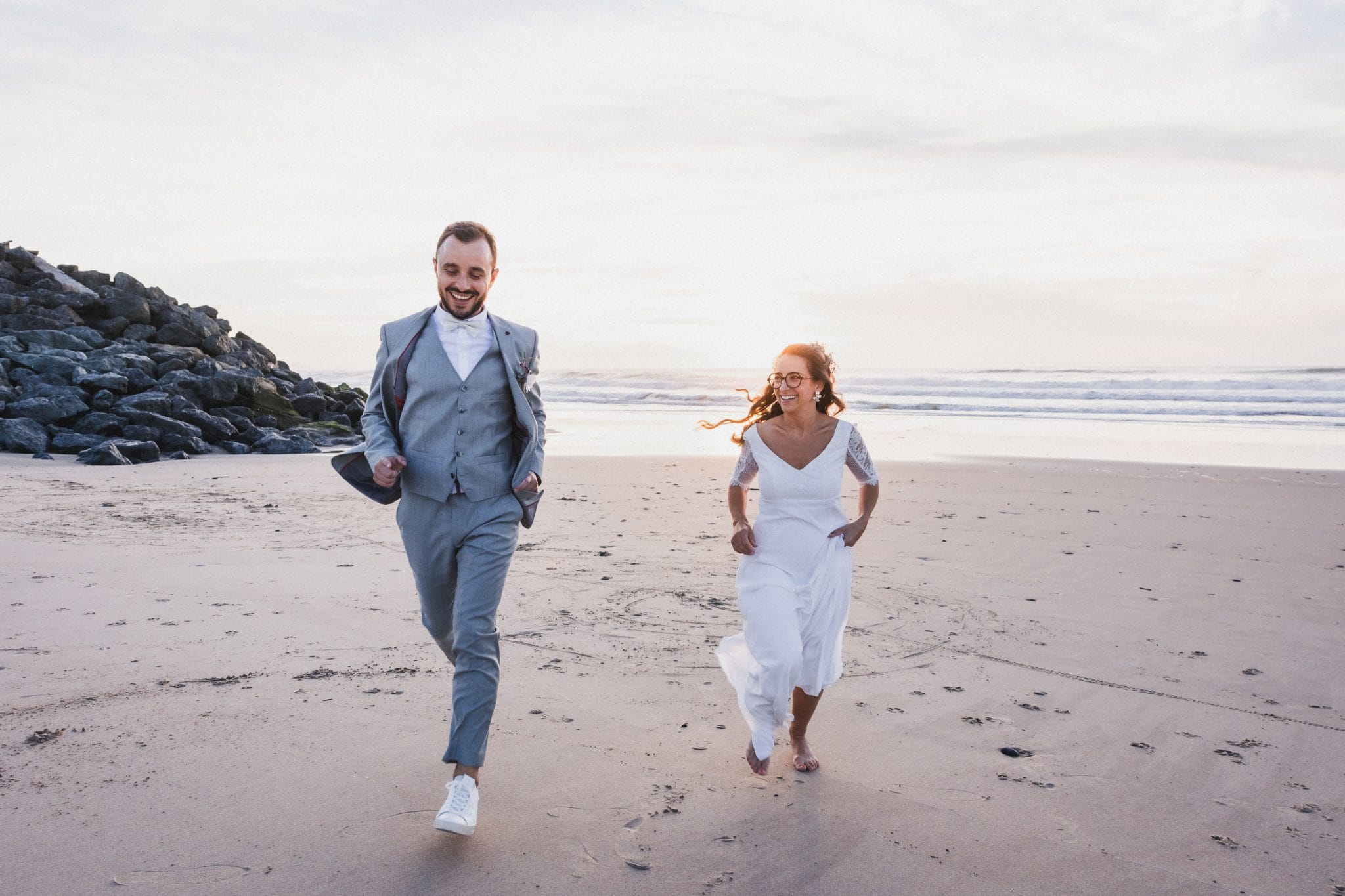 Les mariés courent sur la plage en direction de la photographe pour rejoindre le lieu de leur mariage au Pays Basque