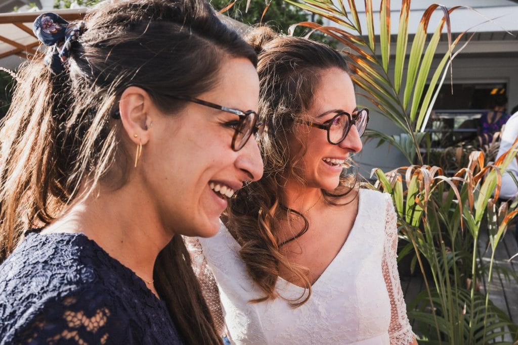 La mariée et sa soeur, de profil, sourient toutes les deux à la sortie de la cérémonie