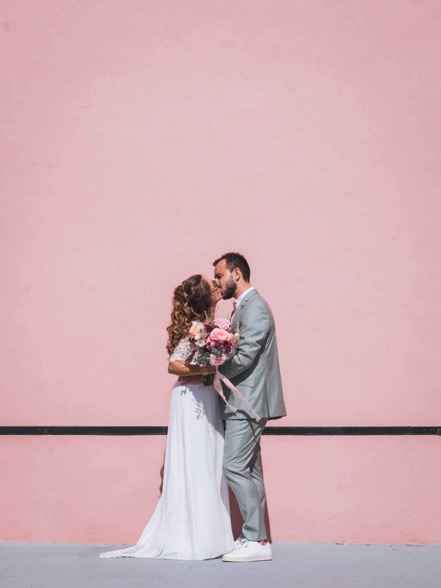 Les mariés s'embrassent devant le fronton rose de la ville de Bardos lors de leur mariage au Pays Basque