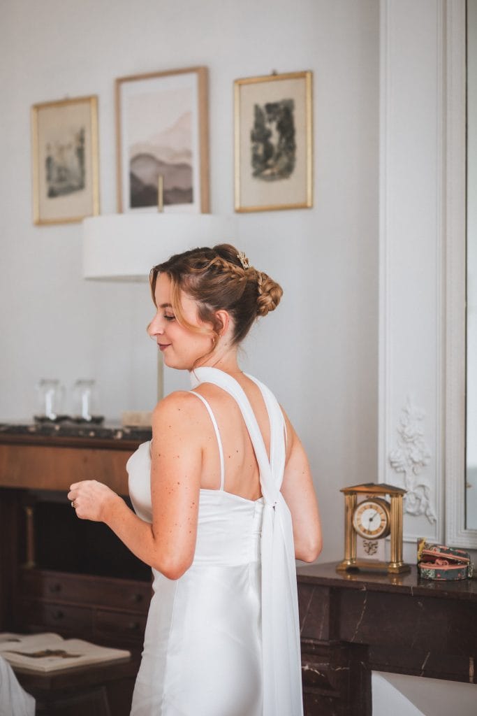 La mariée, fin prête, tourne le dos au miroir en souriant