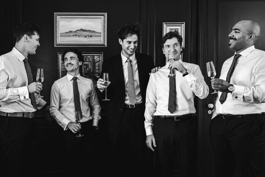 Le marié et ses témoins rient en prenant la pose dans le salon du château avec leurs coupes de champagne