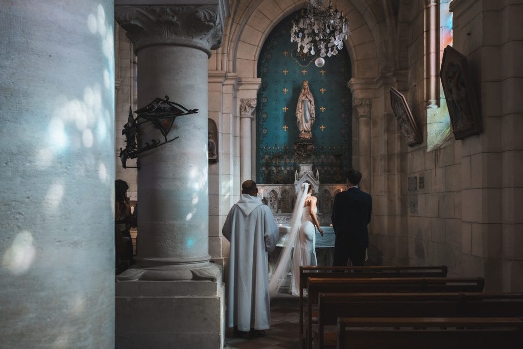 Les mariés déposent le bouquet à la Vierge Marie, la lumière des vitraux diffuse une lumière douce et fragmentée dans l'église