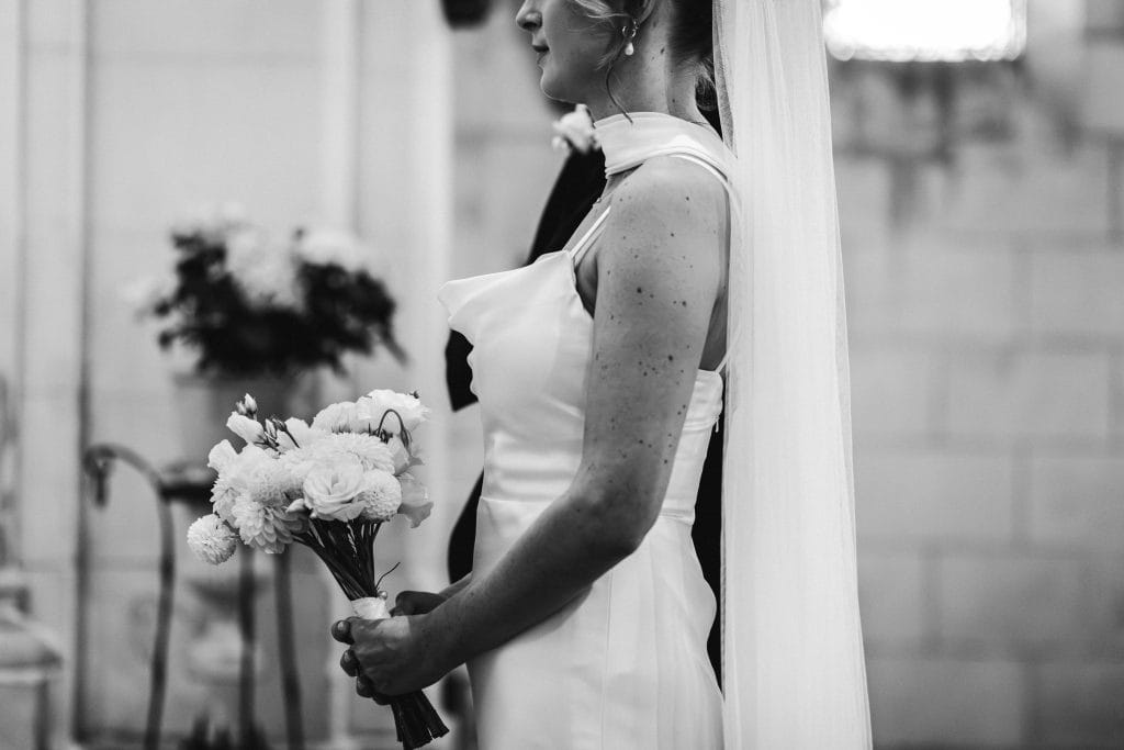 Détail de la robe de la mariée et de son bouquet dans l'église lors de son mariage à Saint-Emilion