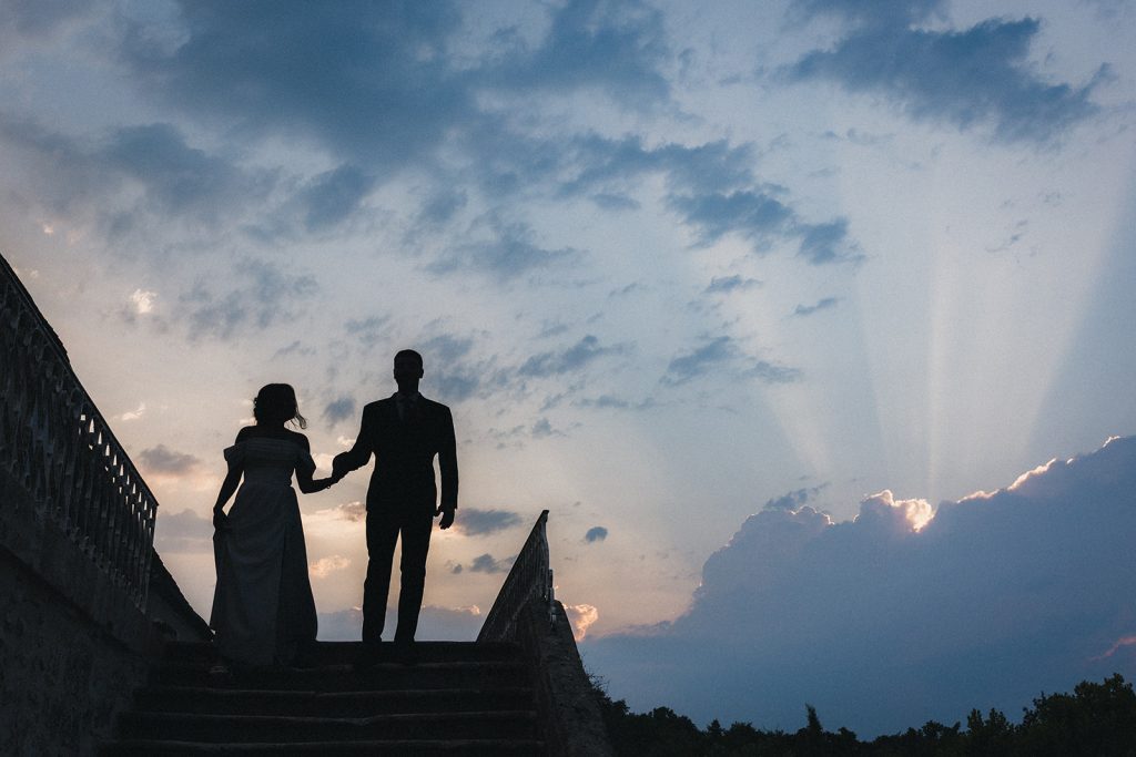 Les mariés, en silhouette, descendent l'escalier du château de Campet, avec en toile de fond un incroyable ciel d'orage.