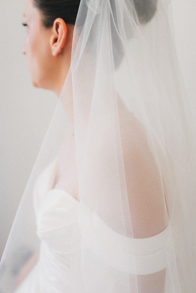 La mariée, tout juste prête, de profil, regarde vers l'extérieur. On distingue à peine son visage.