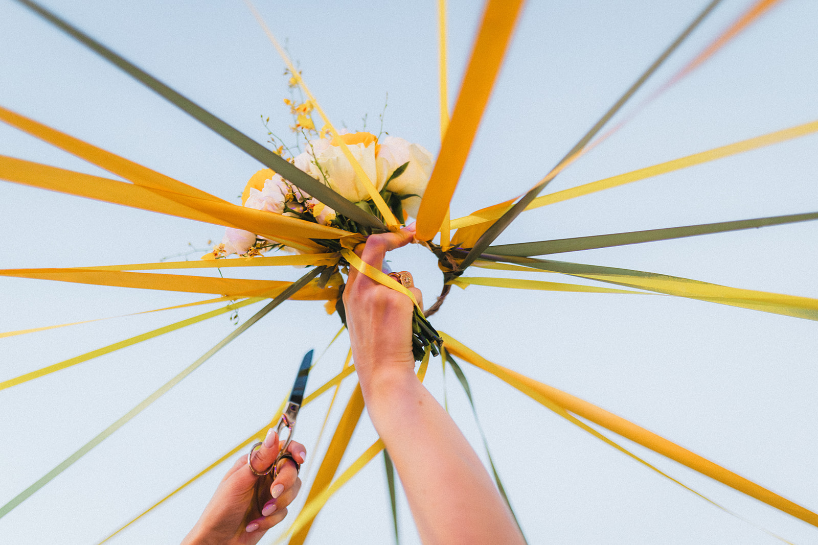 Détail du bouquet de la mariée pendant le jeu des rubans, avec la main de la mariée qui s'apprête à couper un ruban avec les ciseaux